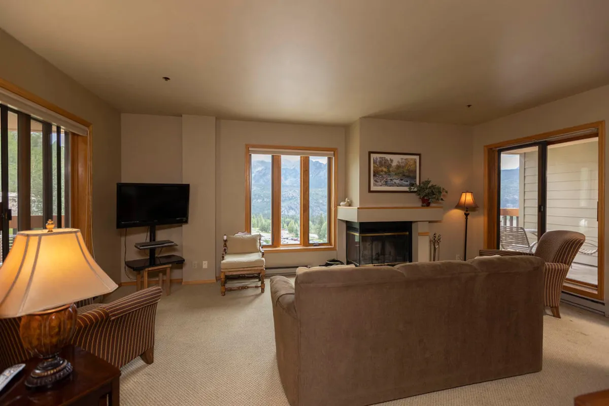 A welcoming living space centered around a fireplace, with large windows framing scenic mountain vistas. Comfortable seating is positioned to encourage socializing, reading, or simply soaking in the relaxing ambiance and breathtaking views.