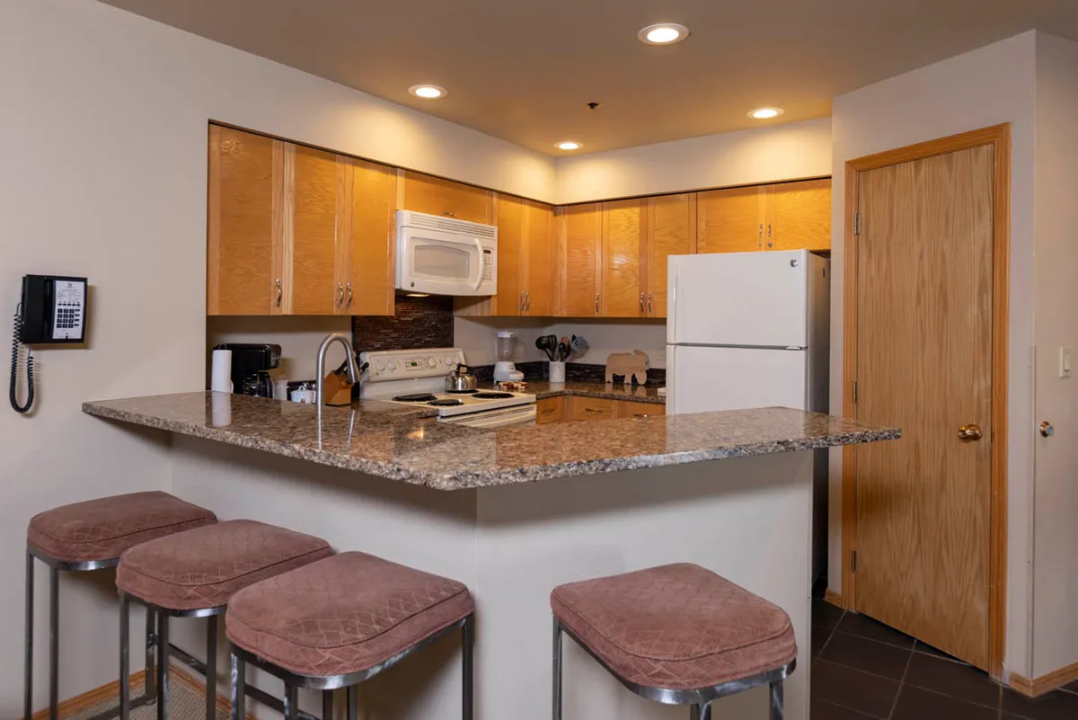 A modern kitchen with granite countertops, bar stools, stainless steel appliances, and wooden cabinetry. The open layout allows for cooking, socializing, and casual snacking, with ample counter space making meal prep enjoyable and communal.