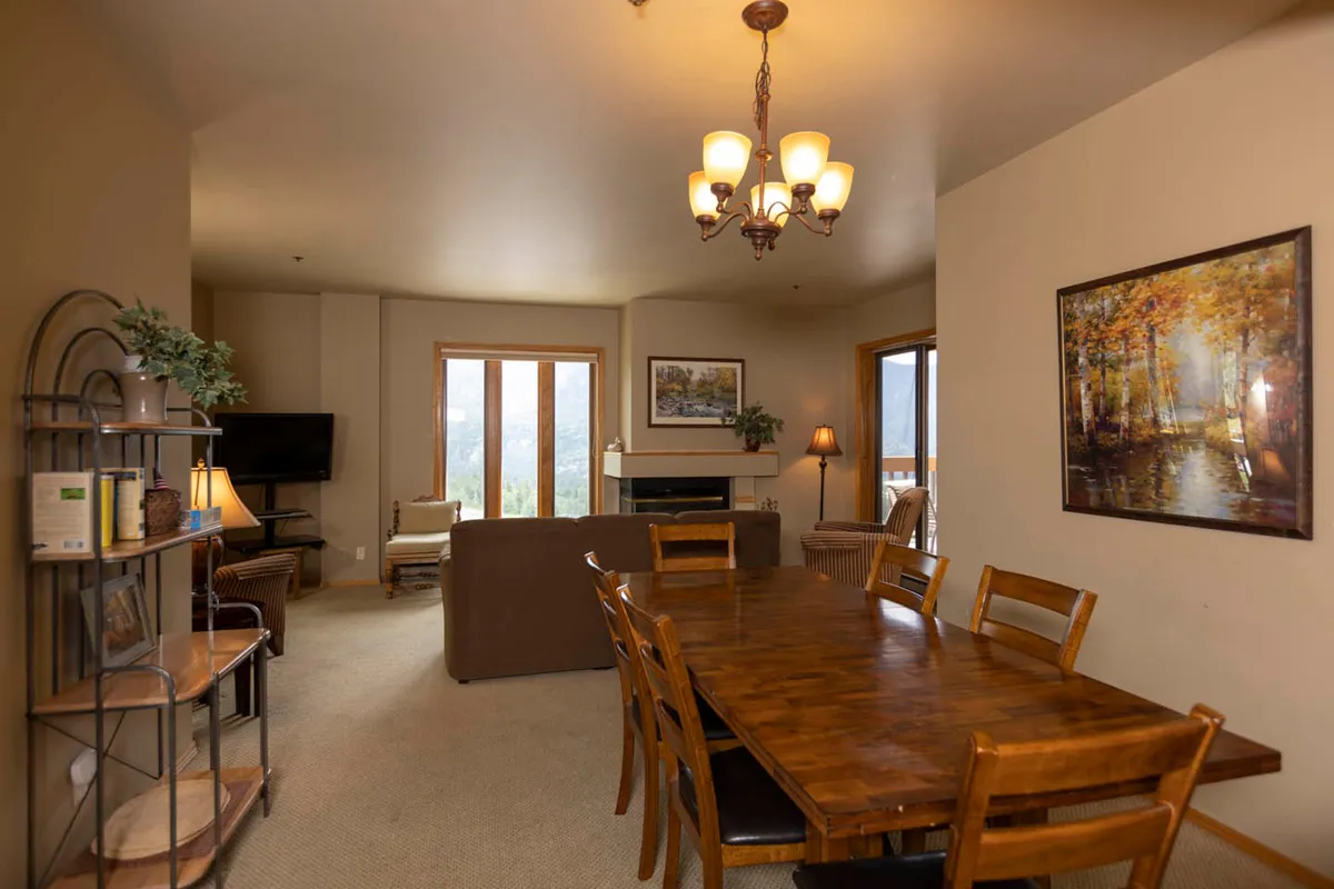 A cozy dining area adjacent to large windows that reveal mountain views. The space features a dining table perfect for family meals or game nights, a chandelier for warm lighting, and artwork on the walls, creating a homey and inviting atmosphere.