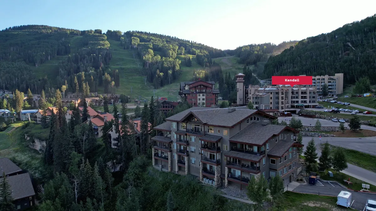 A welcoming exterior view of the lodge with a mountain backdrop, green spaces, and ample outdoor gathering areas. The scene suggests possibilities for hiking, barbecues, and family gatherings against a striking natural setting.