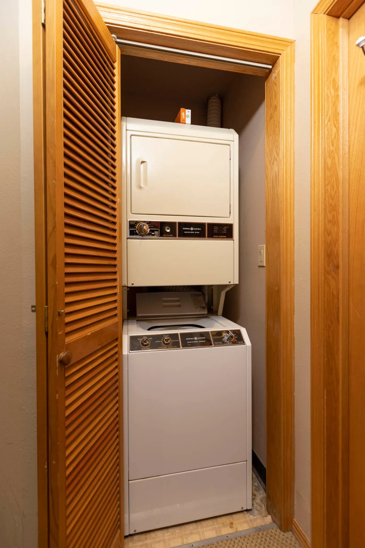A practical laundry room with washer, dryer, and a wooden louvered door, organized for efficiency. The area is clean and clearly designed for convenience and utility.
