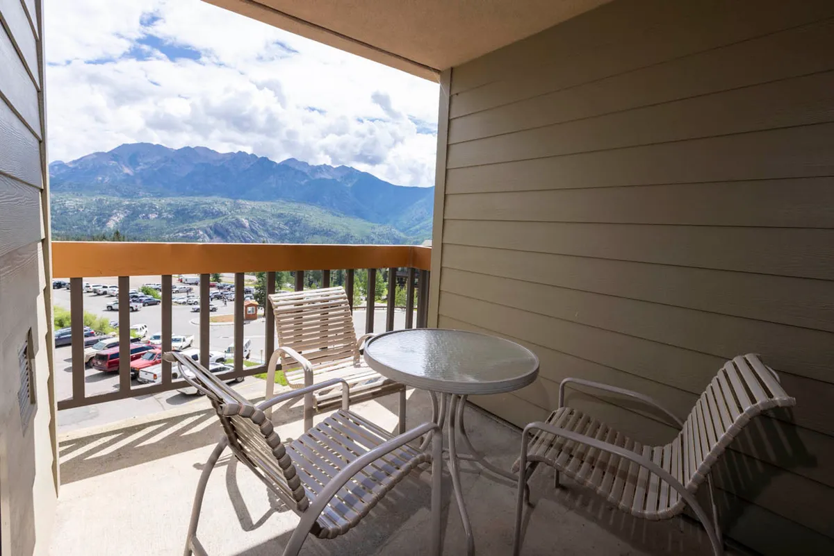 An exterior seating area featuring a table and chairs overlooks a panoramic mountain view, providing an ideal spot for morning coffee or evening relaxation. The peaceful mood and warm lighting evoke moments of connection and shared experiences.