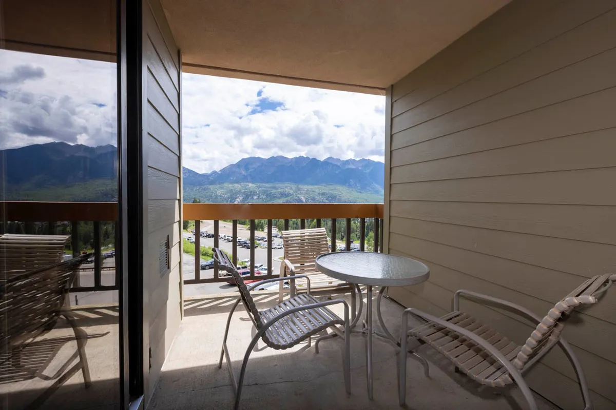 This serene exterior scene presents a balcony with modern furniture and a sleek glass railing, orienting the viewer toward a stunning sunrise or star-filled sky above the mountains. The ambiance is calm and perfect for private relaxation or meaningful conversations.